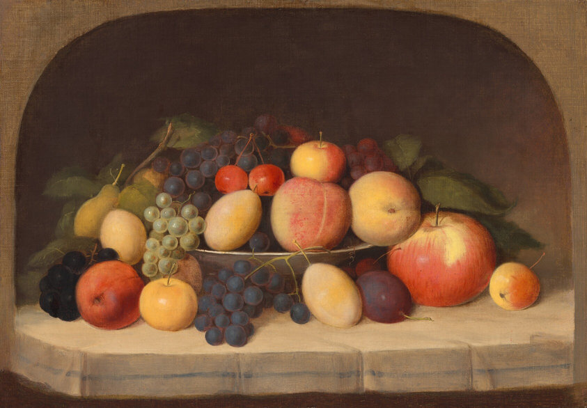 This painting shows various pieces of fruit arranged in a thin white bowl, including apples, peaches, green and purple grapes, cherries, pears, and plums. Some of the fruit is overflowing from the bowl, and rests on the white surface below, surrounding the bowl. Many of the pieces of fruit have thin stems attached to them, and some have thick green leaves. Behind the fruit, the background is dark brown, and there is a tan arched border around the painting.