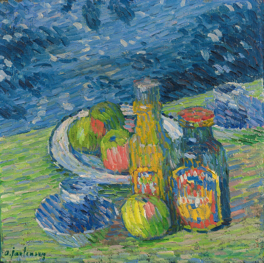 The painting features a collection of fruit on a plate behind two bottles. The plate with the fruit is in the center of the painting, and on it are pieces of round, green fruit with hints of pink. They may be apples. A tall bottle is in front of the plate, and it is yellow with a white cap. Another, shorter bottle is to the right of the first; it has a colorful label. An apple like those on the plate rests in front of the bottles. There are also two blue-gray shapes that could be mugs on round saucers. The surface these objects rest on is mostly green, but there are also streaks of blue and light pink. The wall behind the objects is made up of streaks of light and dark blue. The brushstrokes in the image are thick and visible, blurring the details on the objects.