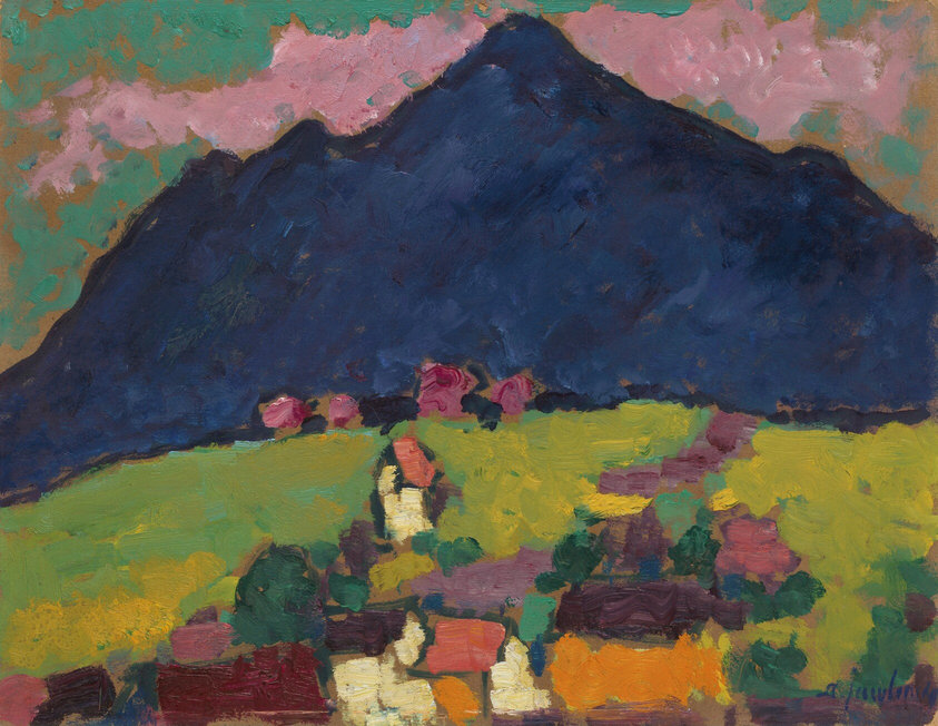 The painting shows a landscape with a large, dark blue mountain in the background. Below the mountain are blocks of color, suggesting fields and structures. The area is filled with colors including yellows, oranges, reds, purples, and greens. The sky above the mountain is painted in a teal color with light pink clouds. The painting features thick brushstrokes, and the shapes lack specific details.