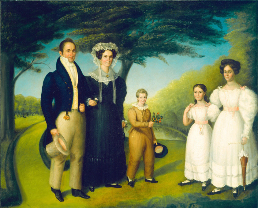 The image shows five individuals standing closely together in a line. On the left is a man in a dark blue coat with a gold emblem, beige trousers, and black shoes. Next to him is a woman in a black dress with a lace collar. In the center is a young boy in a brown suit with gilt buttons. To the right stands a young girl in a white dress with pink ribbons, and a taller woman in a similar dress holding a parasol. The background shows lush green trees and a clear blue sky.